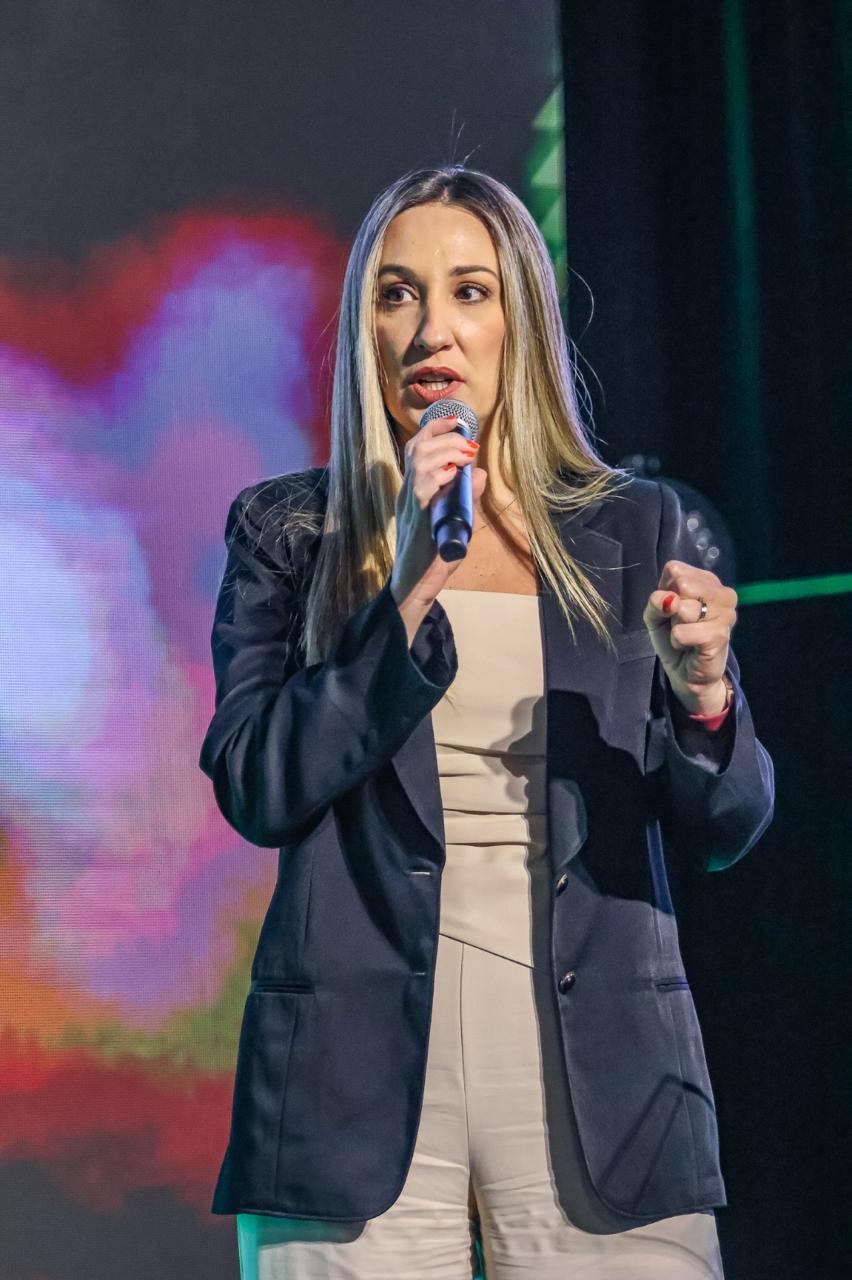 Marusa Trevisan falando ao microfone no palco